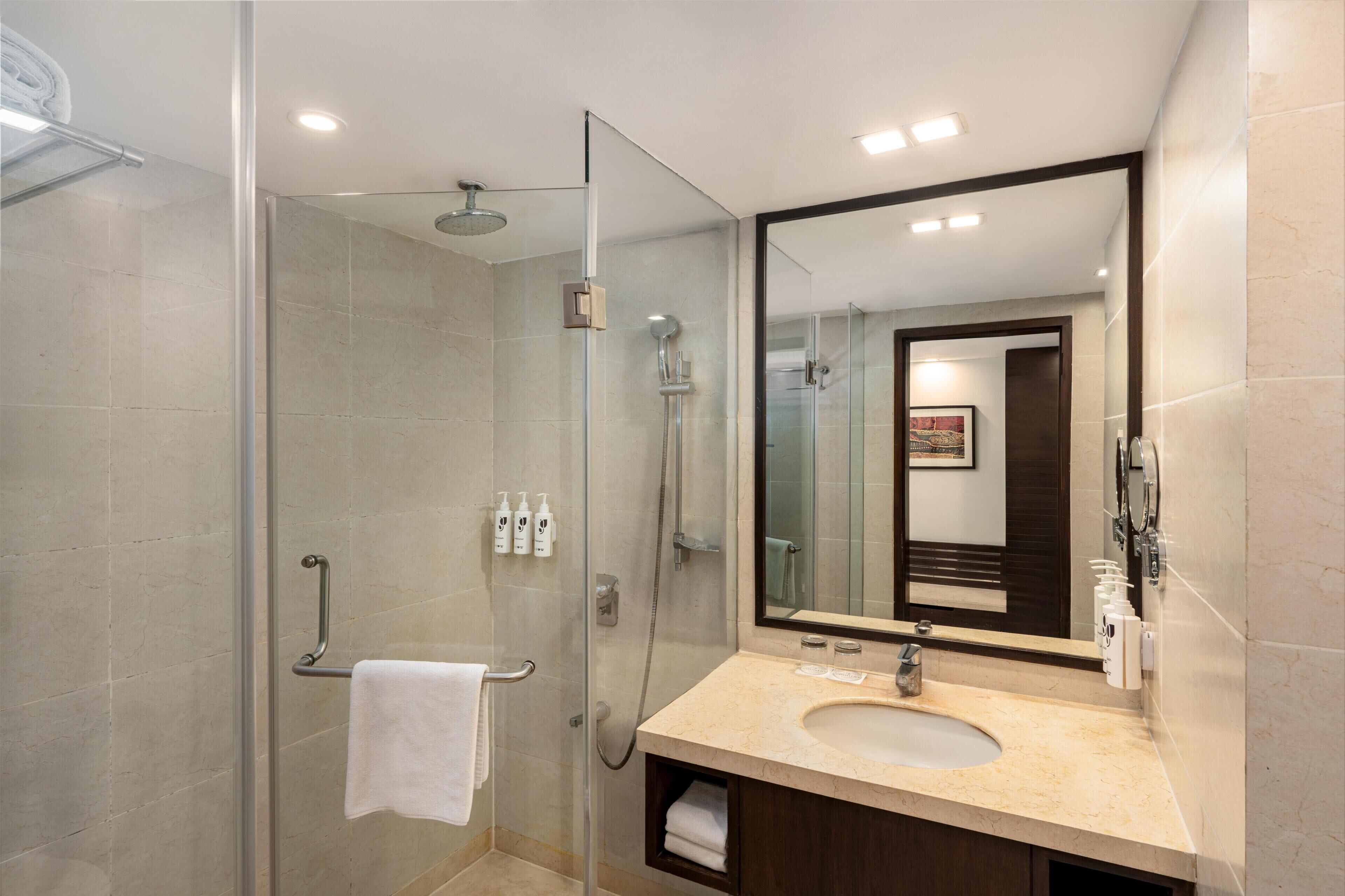 A modern bathroom with a glass-enclosed shower, a sink with a mirror, and toiletries on the wall.