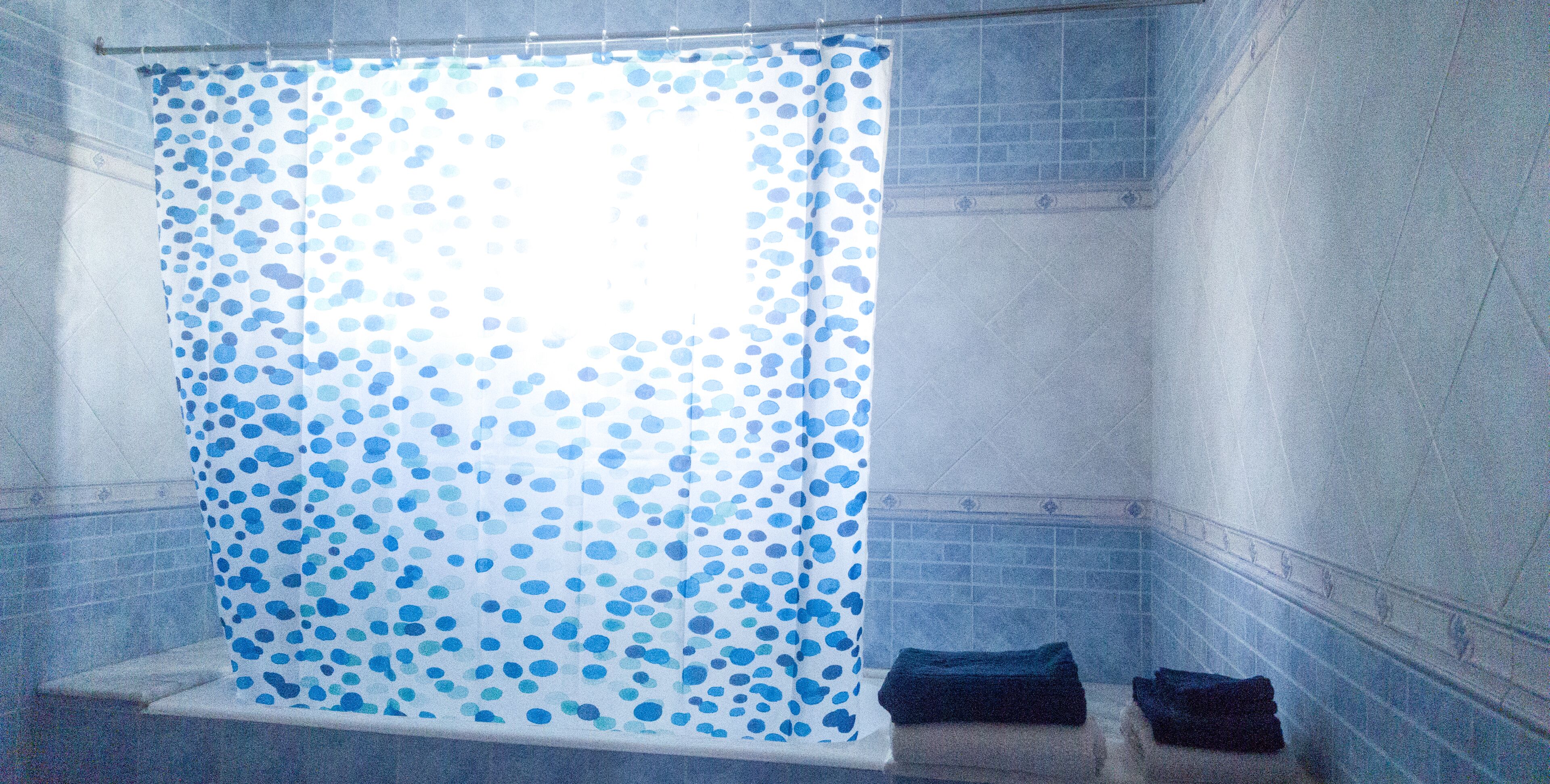 Un bagno con una tenda da doccia a pois blu, una parete piastrellata e un piccolo ripiano con asciugamani piegati.