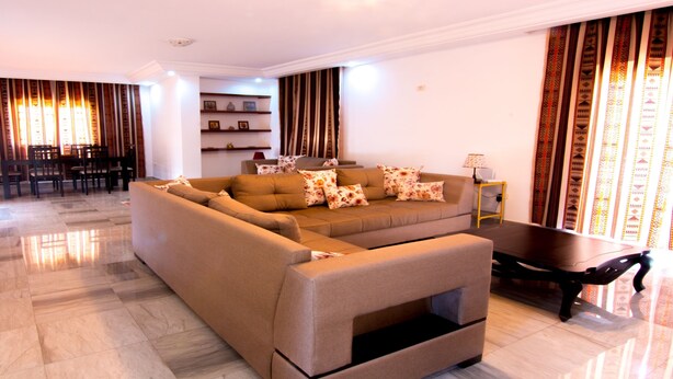 A modern living room with a sectional sofa, a coffee table, and a dining area with chairs and a table. - Mahdia Place Apartments (Mahdia)