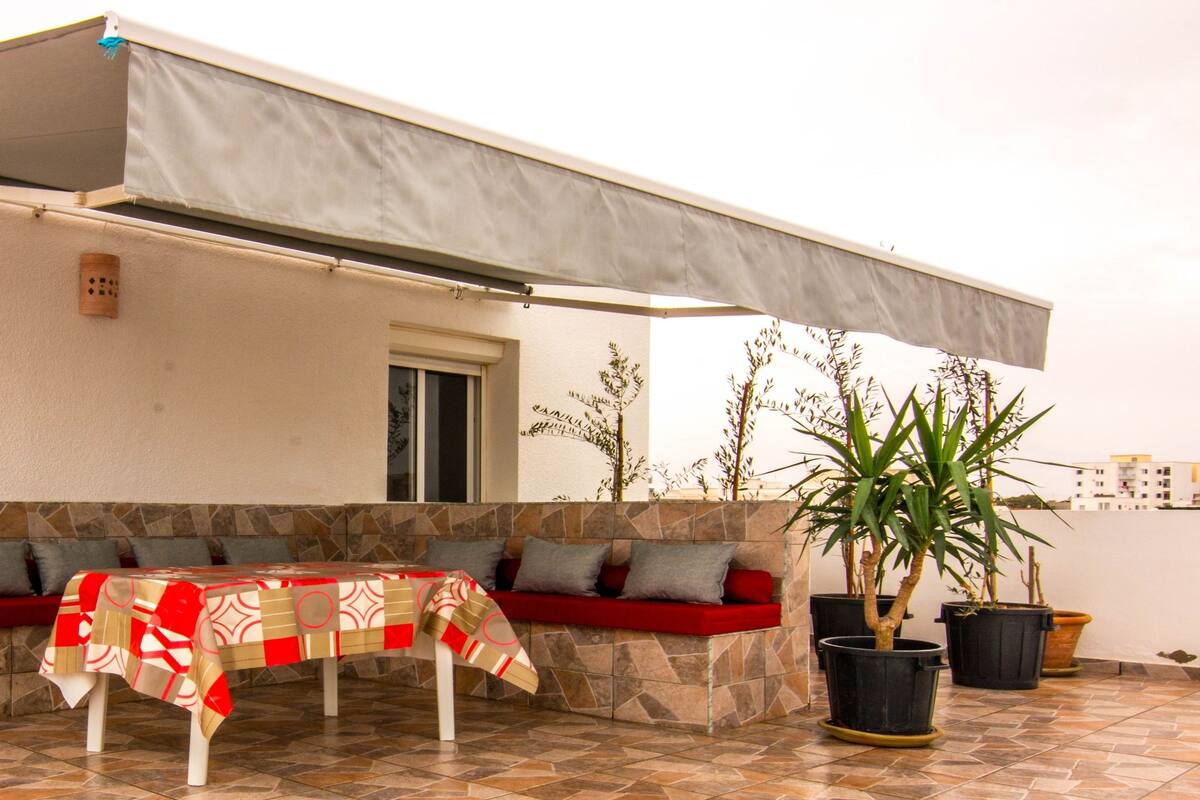 An outdoor seating area with a table and chairs, a covered patio, and potted plants.