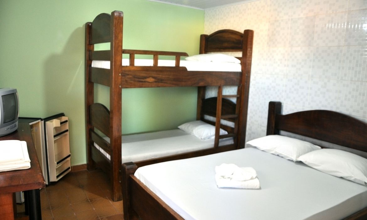 A room with bunk beds, a television, a desk, and a bed with a towel.