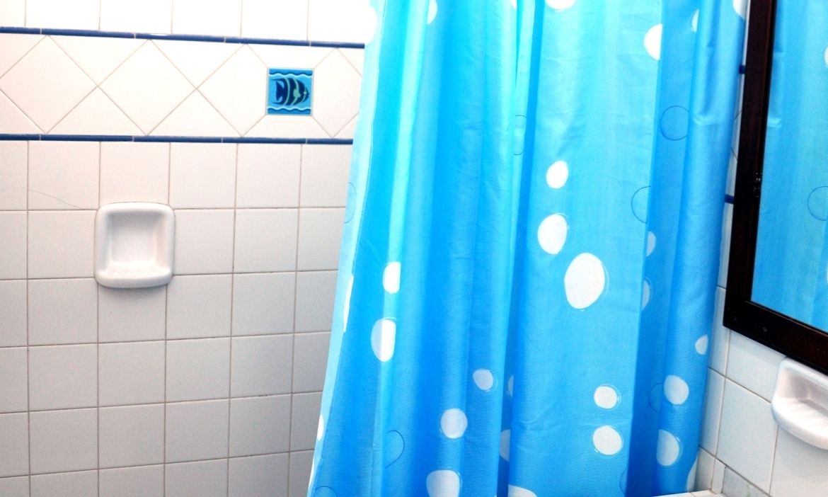 A bathroom with a blue shower curtain with white polka dots, a white soap dispenser, and a tiled wall.