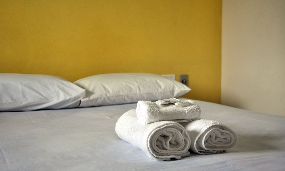 Un lit bien fait, avec des draps et des oreillers blancs, et une serviette enroulée posée sur le dessus.
