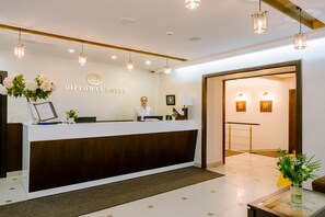 Welcome to the Diplomat Hotel, where guests are greeted by a warm and inviting reception area featuring a beautifully appointed reception desk and elegant decor.