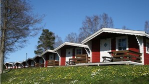 A row of red wooden cabins with white trim and wooden benches on the front porch. - Sikhalls Camping och Restaurang (Bralanda)
