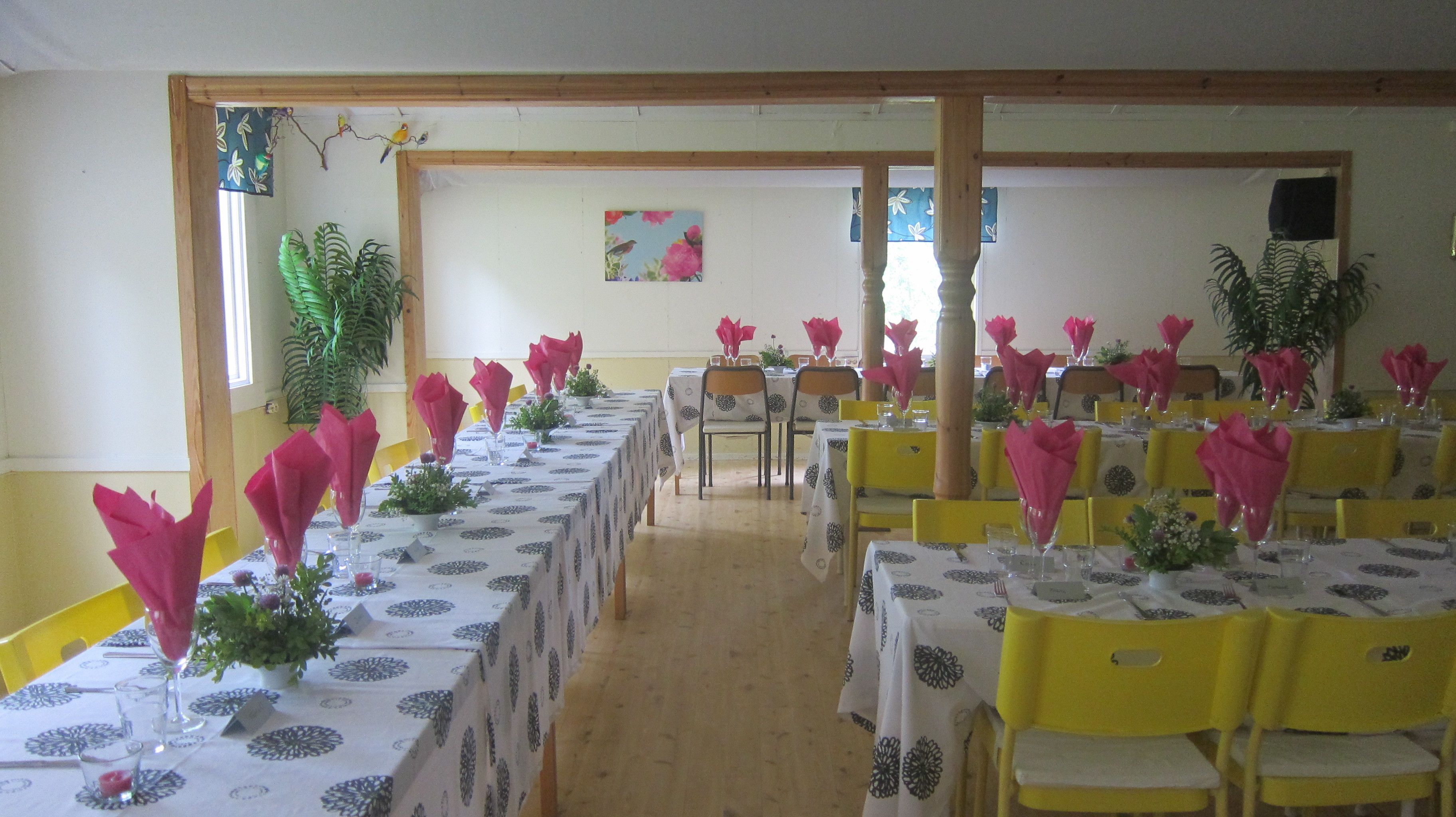 A dining hall with tables set for a meal, yellow chairs, and potted plants.
