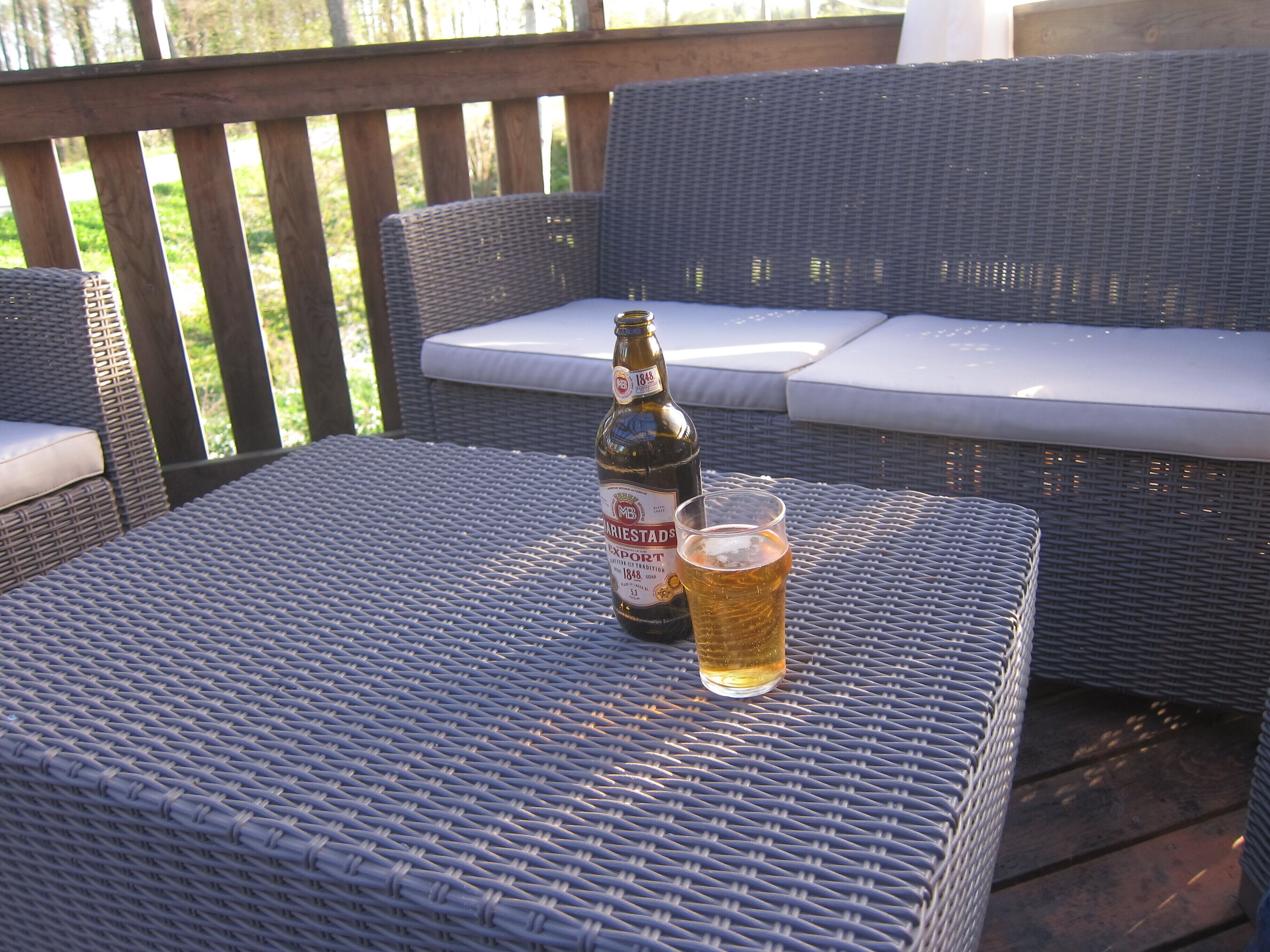 A wicker table with a bottle of beer and a glass on it.