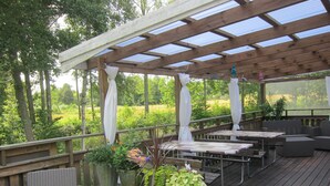 A covered outdoor deck with wooden furniture, a table, and potted plants. - Sikhalls Camping och Restaurang (Bralanda)