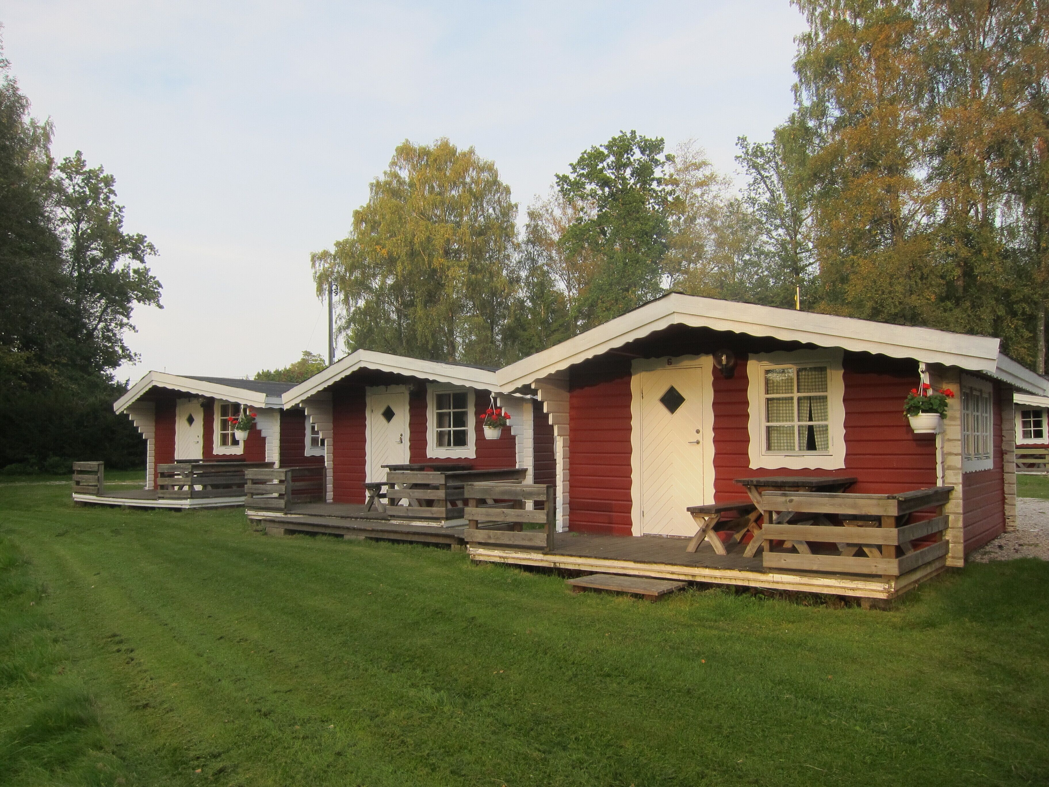 A row of red cabins with white trim, each featuring a porch and a picnic table.