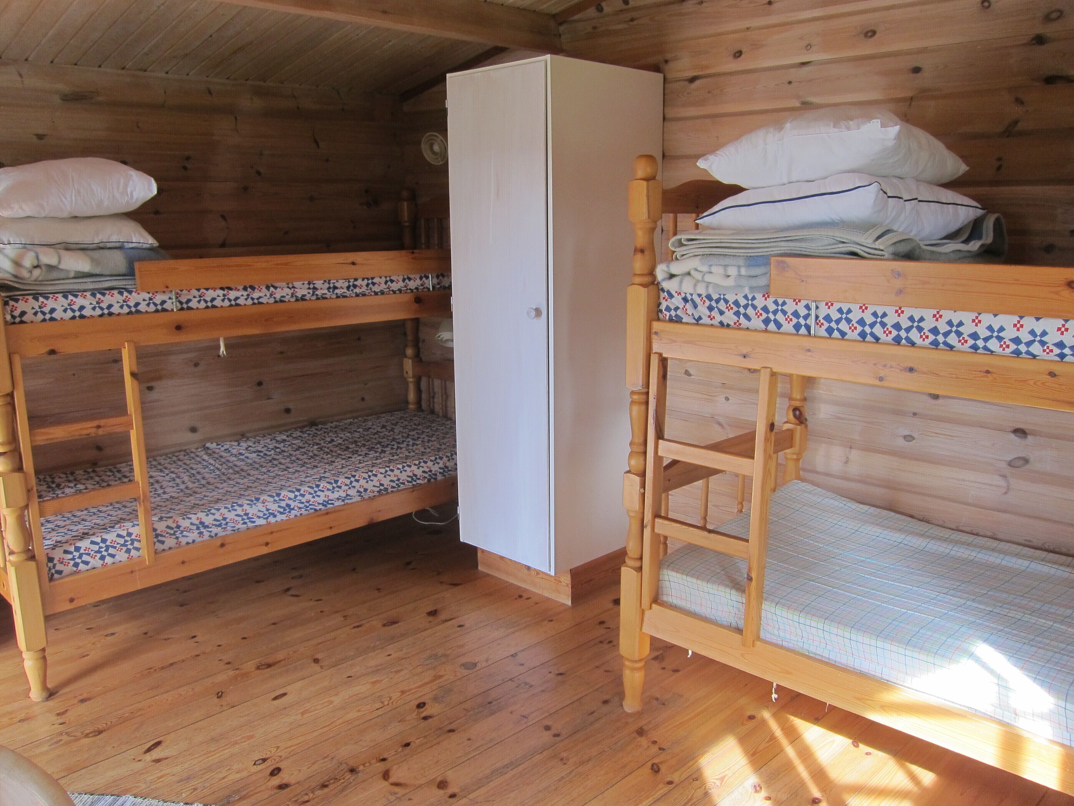 A wooden cabin with bunk beds, a wardrobe, and a fan.