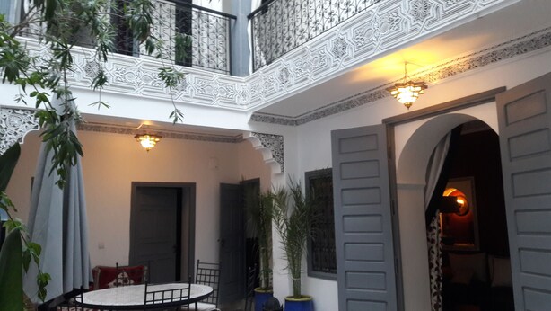 Un patio con una mesa redonda y sillas, una puerta y un balcón con barandillas decorativas.