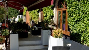 An outdoor seating area with wicker furniture and a red canopy, adjacent to a building with a sign reading "La Bonne Cuisine RESTAURANT". - Hôtel de la Brasserie de Treignac (Treignac)