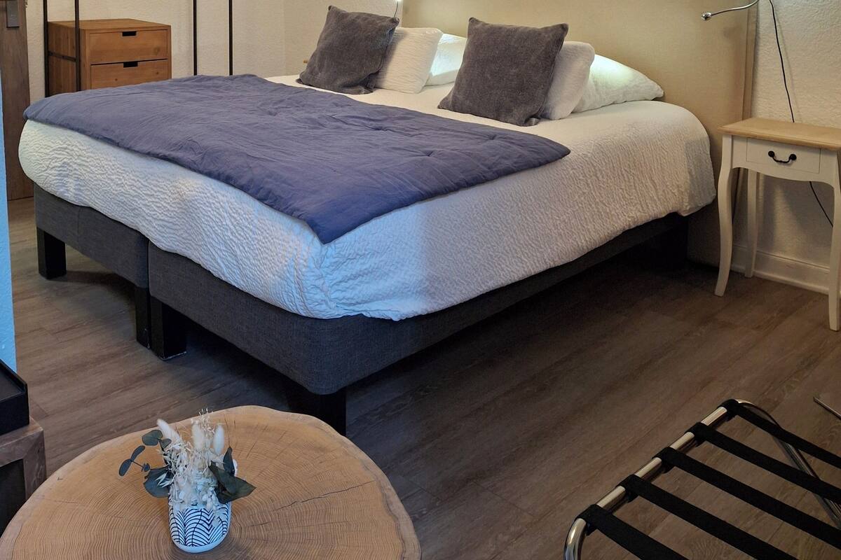 A modern bedroom with a large bed, bedside lamps, a wooden bedside table, and a hanging clothes rack.