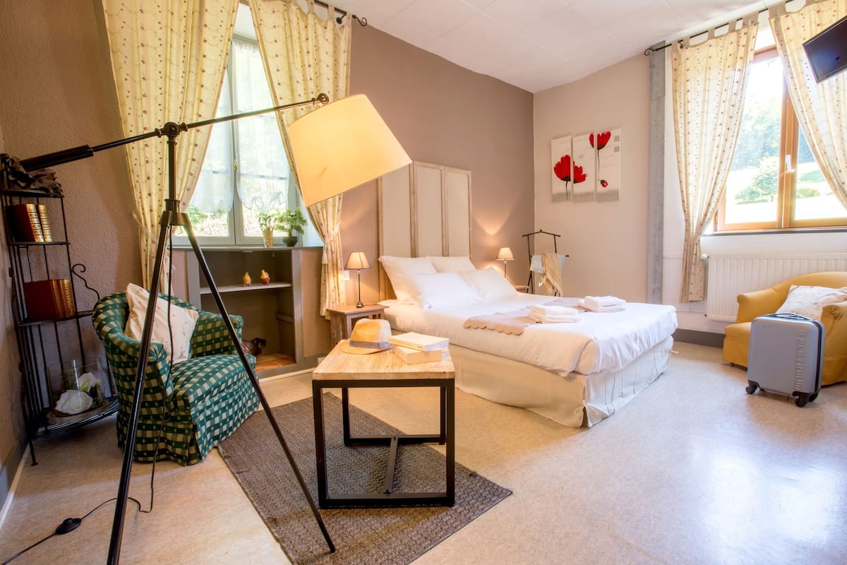 A hotel room with a bed, a chair, a desk, a lamp, and a window with curtains.