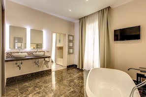 Une salle de bain moderne dotée d’une grande baignoire, de deux lavabos et d’un téléviseur à écran plat fixé au mur.