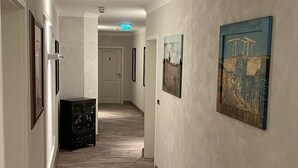 Un couloir au sol en bois, avec des œuvres d’art encadrées accrochées aux murs, et une porte au fond.