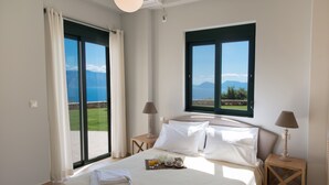 A hotel room with a bed, two nightstands, a window with a view of the sea, and a balcony. - Pearl Mansions (Lefkada)