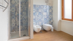 A bathroom with a shower enclosure, two toilets, a bidet, and a window. - Sorrento Coast Relais (Meta)