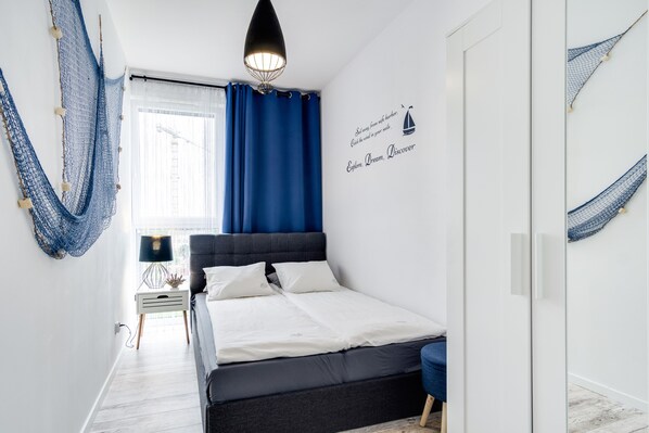 Une chambre à coucher comprenant un lit, une table de chevet, une lampe, une fenêtre avec des rideaux, un hamac et un autocollant décoratif motivant sur le mur.