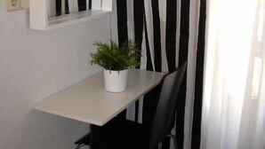A small, white desk with a potted plant, a black chair, and a mirror on the wall. - Hostal On Dormire (Valencia)