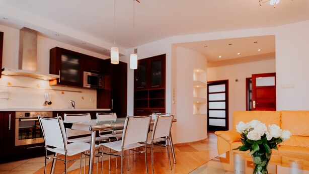 A modern kitchen with stainless steel appliances, a dining area with white chairs, and a living room with a sofa and a vase of flowers. - Elite Apartments Jelitkowski Dwor (Gdansk)