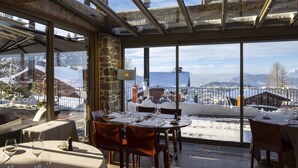 Un restaurant où une table est dressée pour le dîner, avec de grandes fenêtres donnant sur un paysage enneigé.
