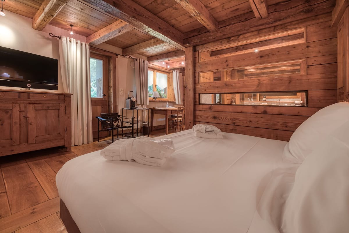 A wooden cabin interior with a bed, a desk, and a TV.