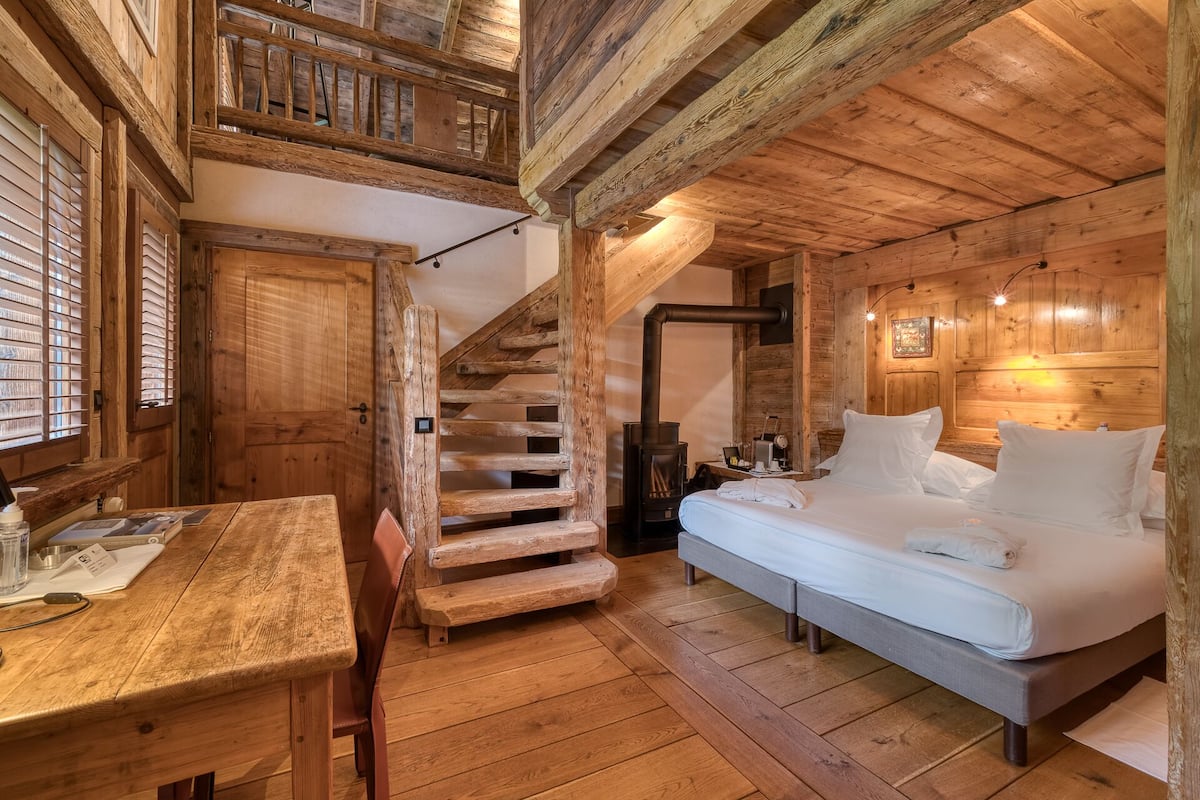 A wooden cabin interior with a bed, a table, and a staircase.