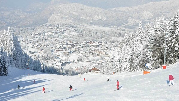 Un centro de esquí nevado con un pueblo de fondo, esquiadores en las pistas y árboles cubiertos de nieve.