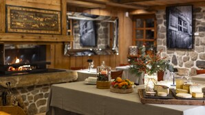 Une pièce chaleureuse avec une cheminée en pierre, des poutres apparentes et une table dressée avec du fromage et des fruits.