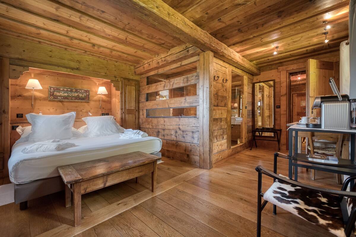 A wooden cabin-style room with a bed, bench, and a table with a kettle.