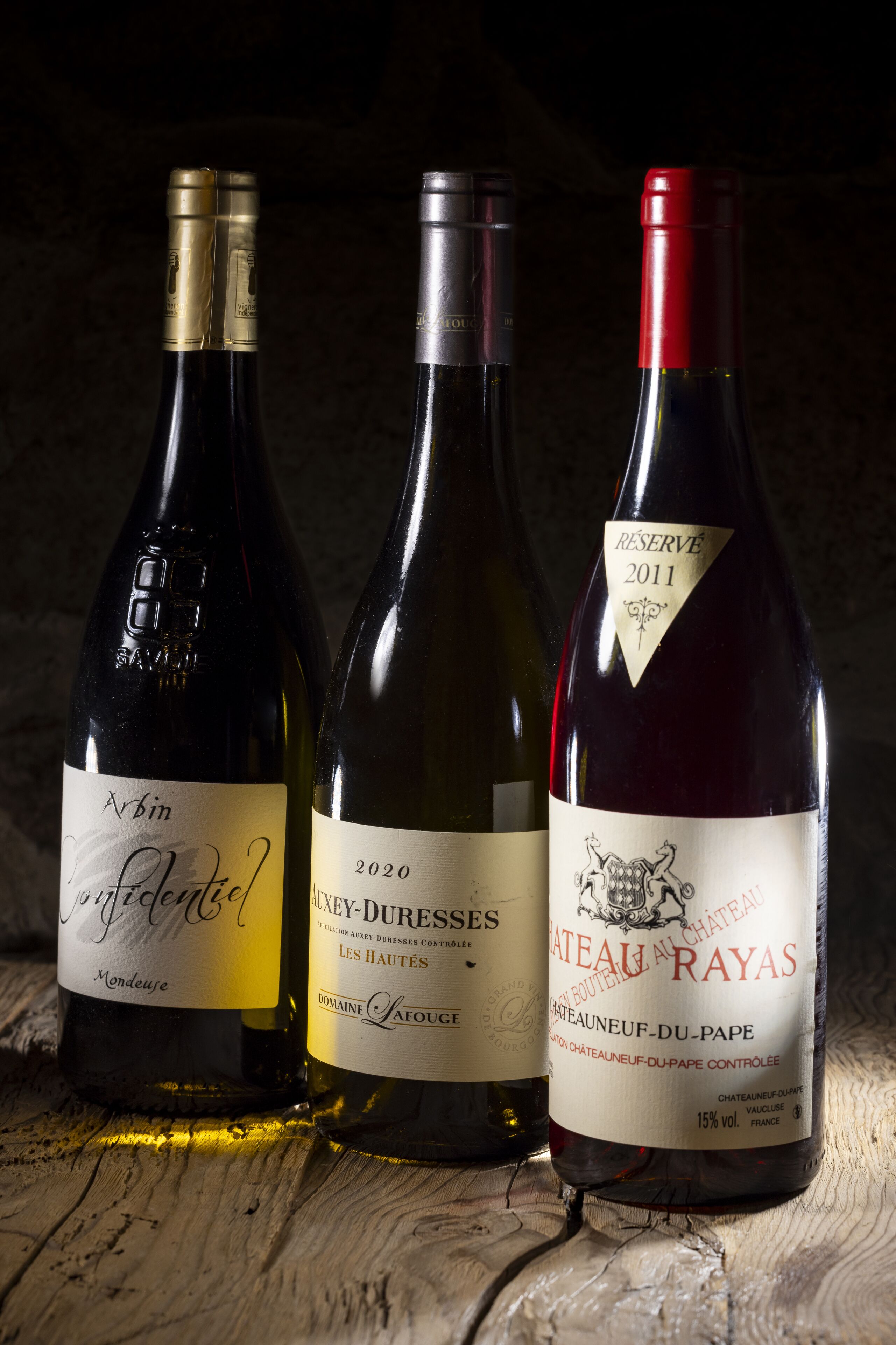 Three wine bottles on a wooden surface.
