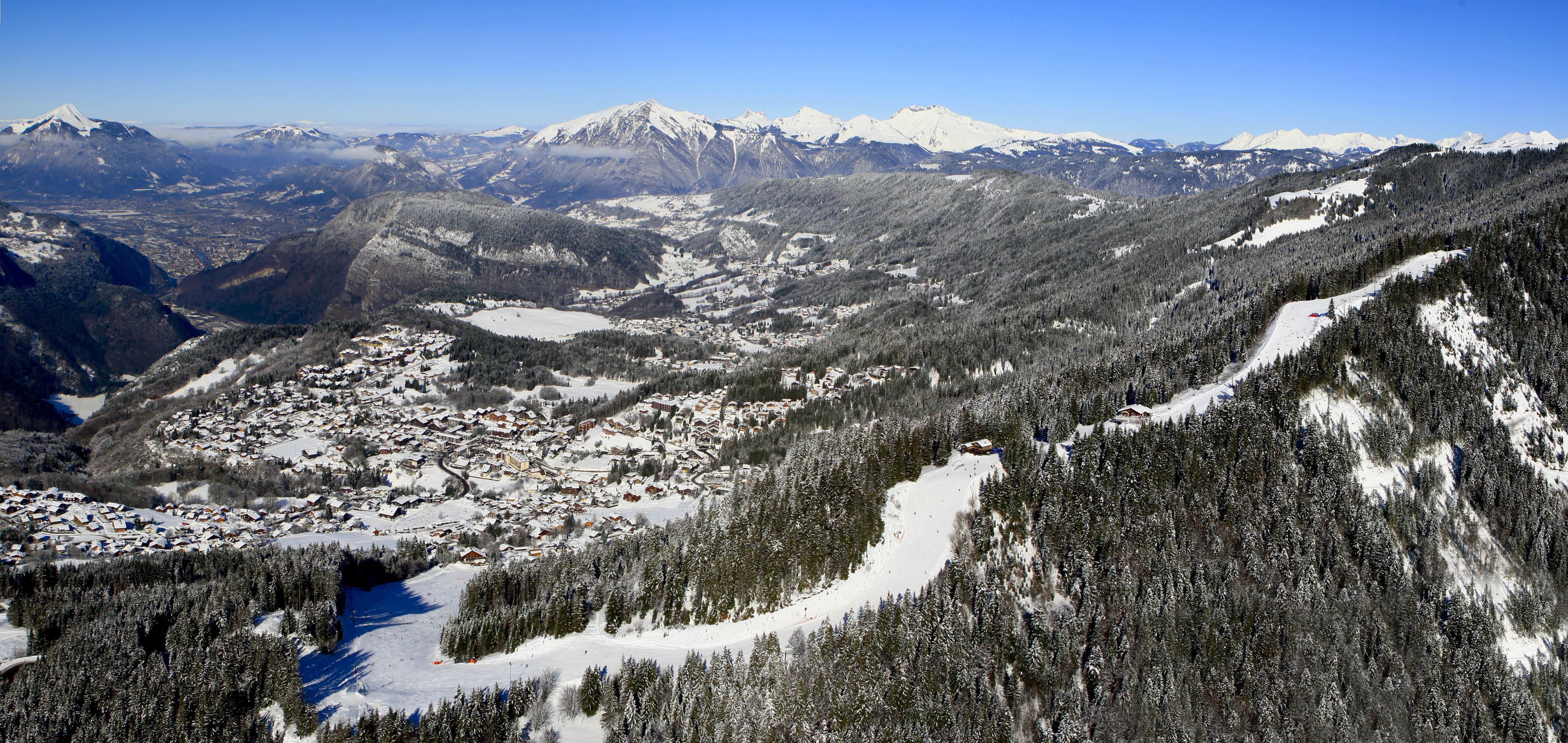 A snow-covered mountain town with a ski resort, dense forests, and a clear blue sky.