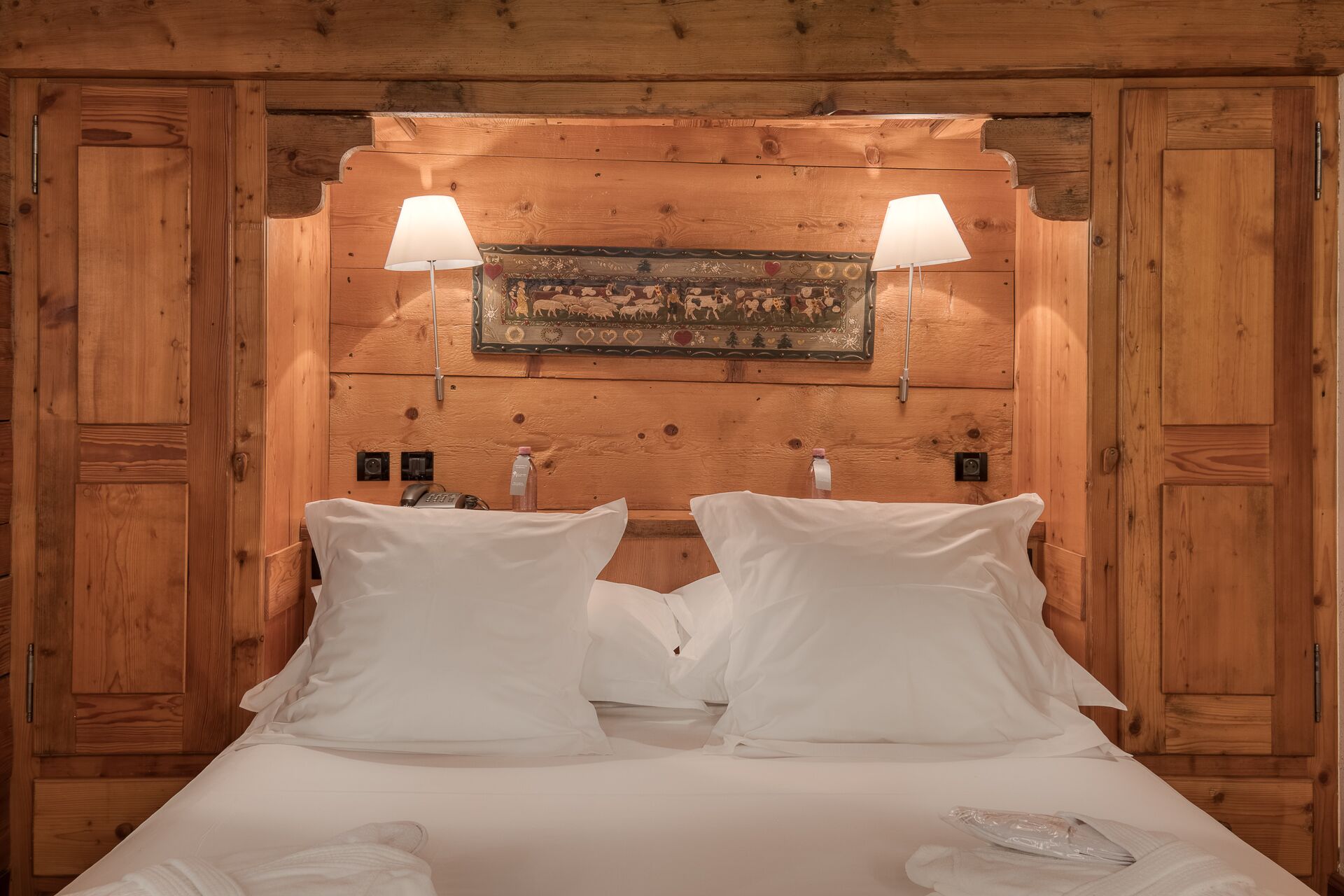 A wooden-paneled bedroom with two bedside lamps, a framed picture above the bed, and a bedside telephone.