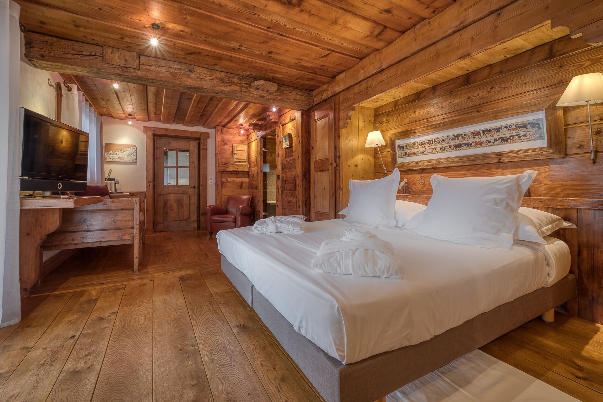 Ein schlicht eingerichtetes Schlafzimmer im Chalet-Stil mit einem großen Bett, einem Schreibtisch und einem Fernseher.