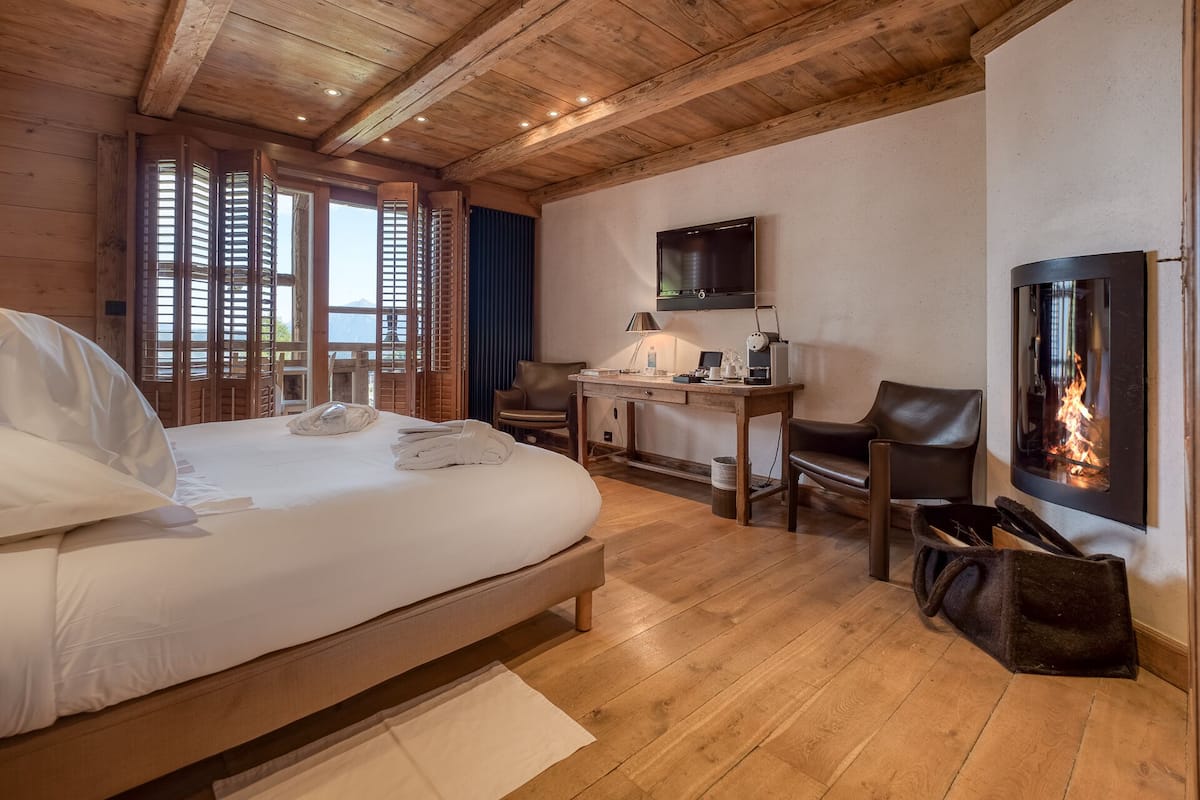 A bedroom with a bed, desk, chair, and a fireplace.