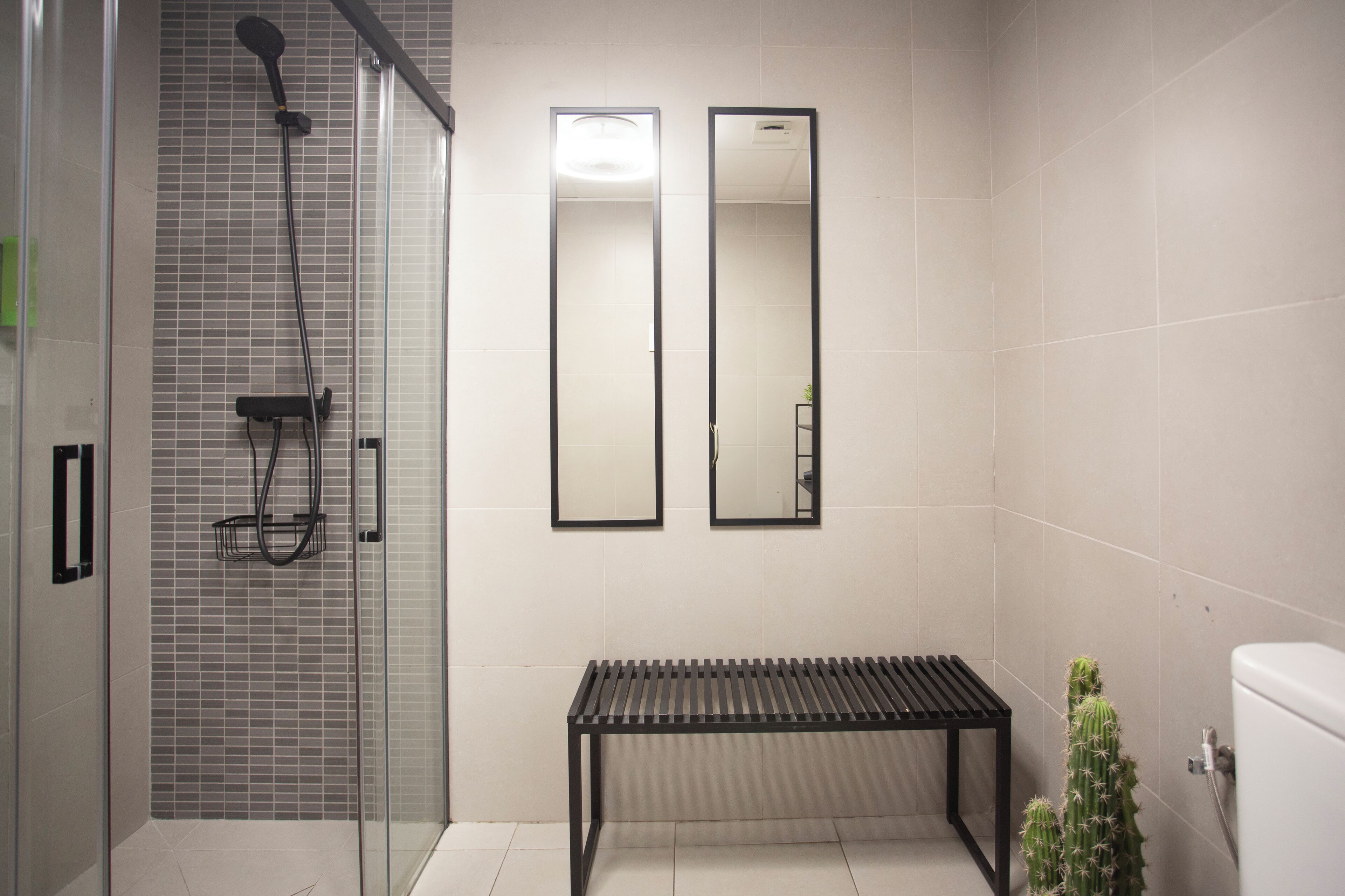 Un baño moderno con cabina de ducha de vidrio, un banco y dos espejos.