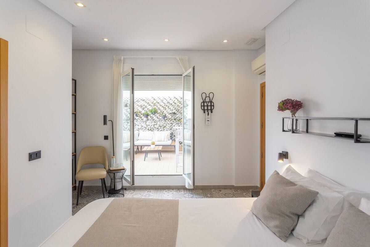 Ein modernes Hotelzimmer mit einem großen Bett, einem Sessel, einem kleinen Tisch und Blick auf eine Terrasse.