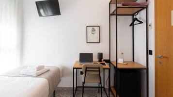 Una habitación de hotel con cama, escritorio con computadora portátil, silla, mueble pequeño, televisor montado en la pared y una puerta.