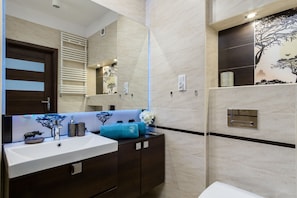 A modern bathroom with a large mirror, a white sink, dark wooden cabinets, and a decorative tree mural on the wall.
