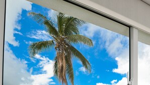A view through a window of a palm tree, a clear sky, and a body of water. - The Sanctuary at Los Corales (Punta Cana)