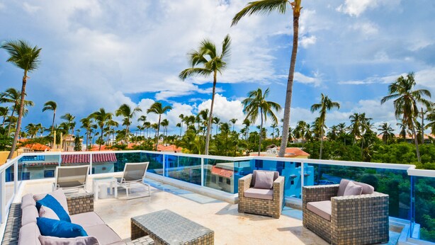 A poolside area with wicker furniture, a glass-enclosed pool, and palm trees in the background. - The Sanctuary at Los Corales (Punta Cana)