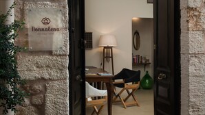 A boutique hotel entrance with a stone wall, a signboard, a wooden table with chairs, a lamp, and a staircase leading to another room. - Nonnalena Hotel (Chania)