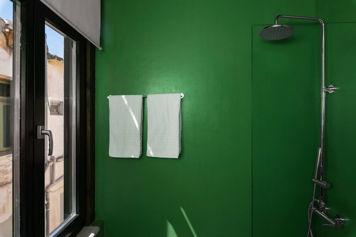 A bathroom with a green wall, a window, and a shower.