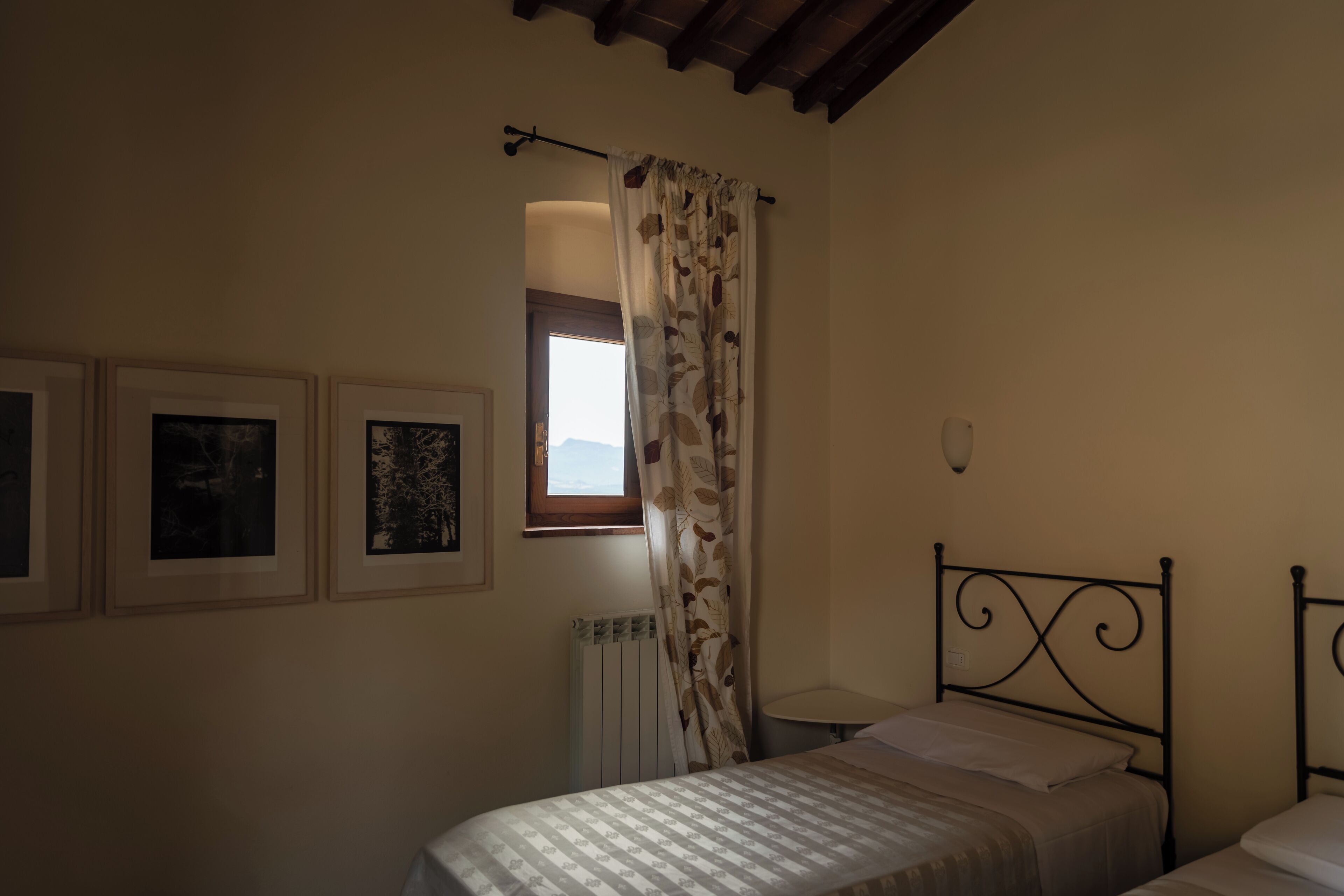 Un dormitorio con cama, ventana con cortinas y dos cuadros en la pared.