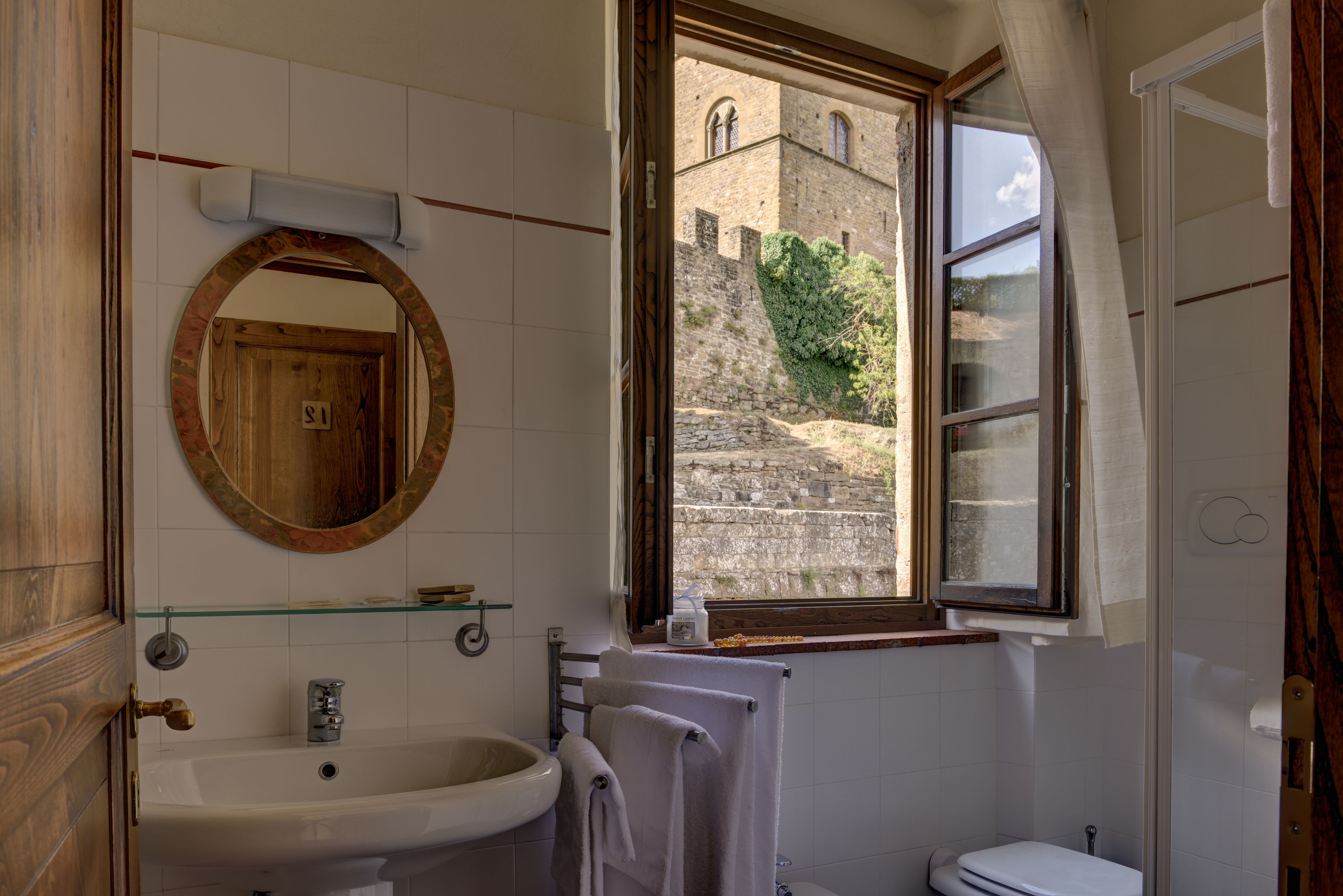A bathroom with a sink, mirror, and window overlooking a stone building.