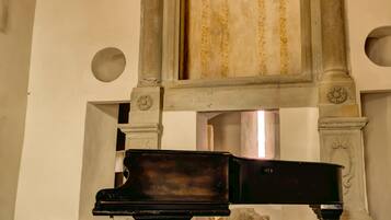 Un gran piano en una habitación amplia con una chimenea grande y ornamentada, un taburete pequeño y una escultura de piedra.