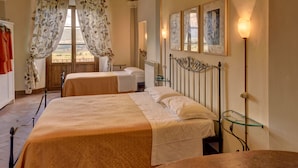 A room with two beds, a wooden table, a glass shelf, and a view of the outdoors. - Albergo San Lorenzo (Poppi)
