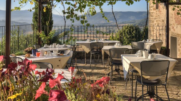 An outdoor dining area with tables and chairs, a pergola, and a view of distant mountains. - Albergo San Lorenzo (Poppi)