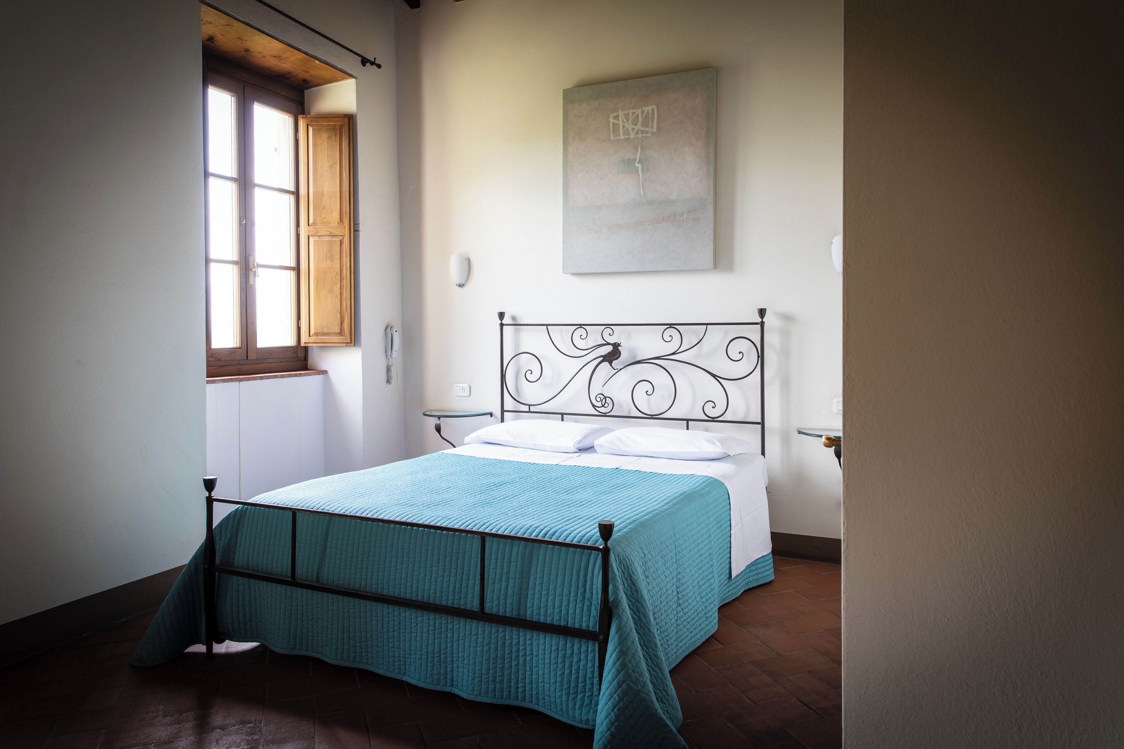 Une chambre à coucher avec un lit, une fenêtre, une œuvre d’art accrochée au mur et une table de chevet.